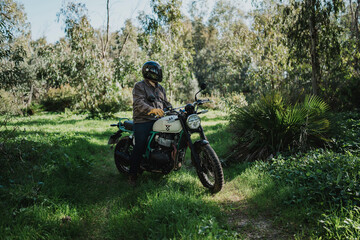 Hombre aventurero con barba en moto estilo scrambler en el bosque en dia soleado