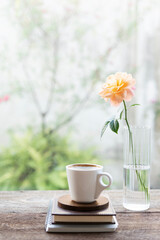White coffee cup and diary notebook and glass vase of rose