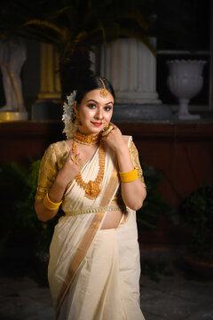 Indian bride wearing a traditional saree and gold jewellery stands before a vintage background