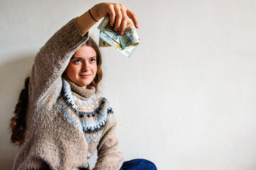 Young woman holding euro banknotes against blank wall with copy space
