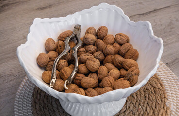 White ceramic bowl filled with whole walnuts and vintage metal nutcracker