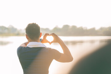 The young man made a heart shape with both hands above his head, with his back turned, and was in love. He made a heart shape with both hands.