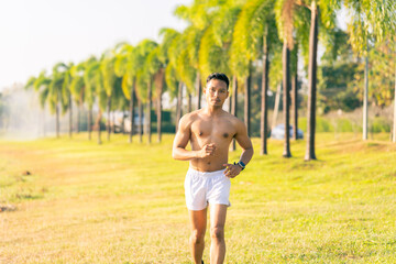 A young Asian man is jogging outdoors in a park in the morning. The concept of exercise for health is depicted.