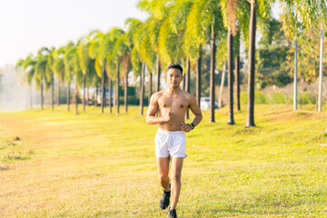 A young Asian man is jogging outdoors in a park in the morning. The concept of exercise for health is depicted.
