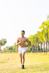 A young Asian man is jogging outdoors in a park in the morning. The concept of exercise for health is depicted.