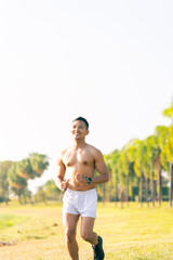 A young Asian man is jogging outdoors in a park in the morning. The concept of exercise for health is depicted.