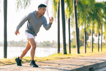 A young Asian man is jogging outdoors in a park in the morning. The concept of exercise for health is depicted.