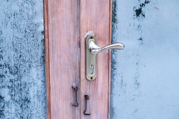 Close-up of a metal handle on a wooden door with frosted glass and ice, capturing the cold winter atmosphere.