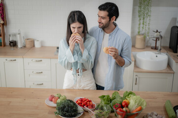 Happy young couple enjoying eating homemade burgers together in the kitchen.