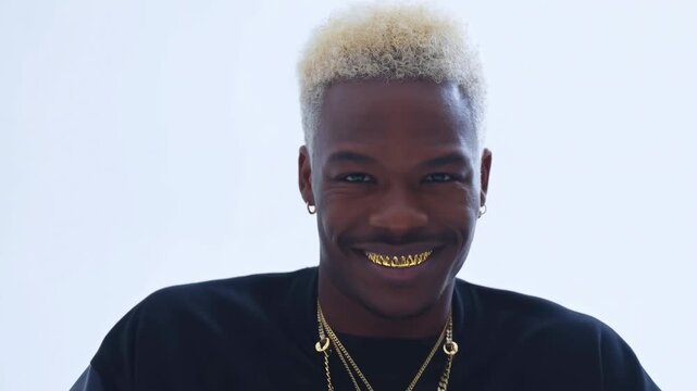 Stylish young man smiling with gold teeth and blonde hair against light background