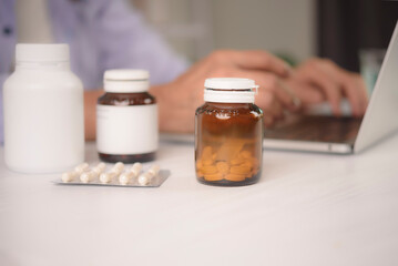 Close up medicine bottles, vitamin supplement and blister pack on table. Senior woman using laptop for ordering prescription pharmacy online or consulting doctor via telemedicine .