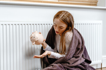 Young woman sitting on the floor with a piggy bank looking at her empty hand during winter