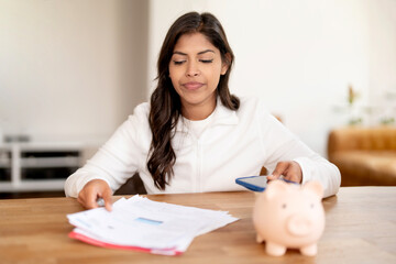 Woman managing financial documents and checking expenses with a phone at home