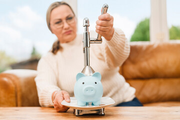 Woman using a kitchen tool to press down on a piggy bank on a wooden table near a couch