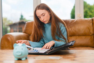 Teen student reviews notes while sitting at home with a piggy bank on the table