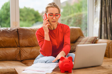 Woman makes a phone call while managing finances at home with a laptop and documents