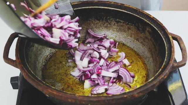 Sliced red onions are fried in vegetable oil in a deep cast-iron skillet