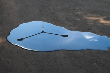 A puddle on an asphalt road with a reflection of a lamppost and blue sky. Shallow depth of field