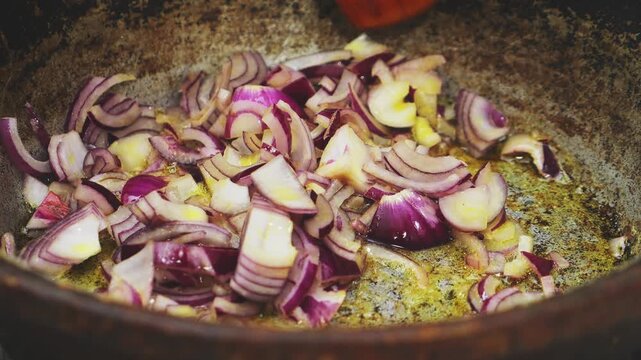 In a deep cast-iron skillet, chopped red onion is fried in vegetable oil