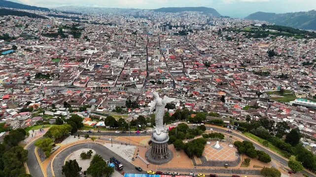 Aerial drone footage of El Panecillo hill featuring the iconic Virgin of Quito statue overlooking the city of Quito, Ecuador. Important cultural and religious landmark with panoramic views of the capi