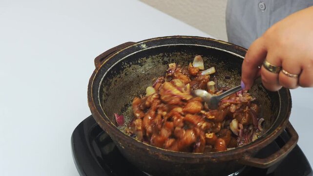 In a deep cast-iron skillet, onions are fried in vegetable oil with chicken marinated