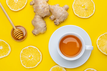 Warm cup of tea with ginger, honey, and lemon slices on a bright yellow surface
