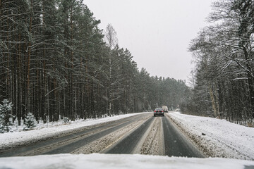 Russia, Saint Petersburg, 11.01.2026 Dirty winter road with cars driving through snow and dense forest. View from inside a car on a dangerous snowy highway. Traveling concept.