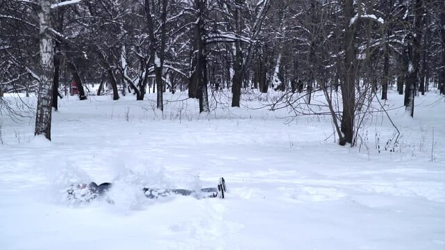 slow motion close up of bearded man in blue puffer jacket and fur hat falling backward into deep fresh snow in winter forest with arms and legs spreading out creating joyful playful winter moment 