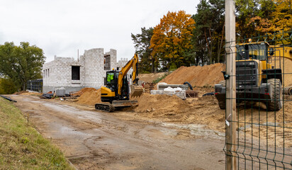 Rogachev, Belarus - October 8, 2025 - Yellow excavator against the backdrop of a brick building under construction and a pile of sand