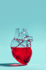 Realistic red glass human heart filled with water in a surreal minimalist concept on a vivid mint background