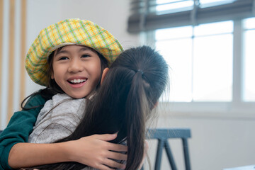Two young student girls share a warm hug indoors, expressing friendship, happiness, and emotional connection in a bright, cozy classroom environment. Back to school