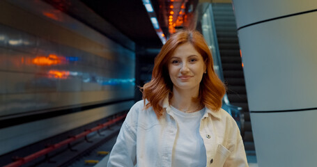 Redheaded woman waits on subway platform in urban setting