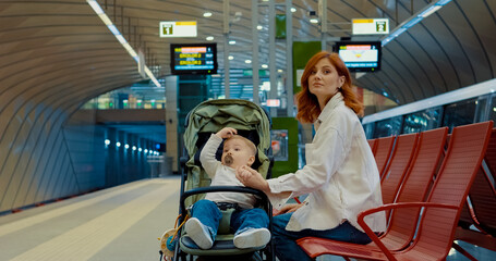 Mother with baby waits for subway at station bench during busy commute