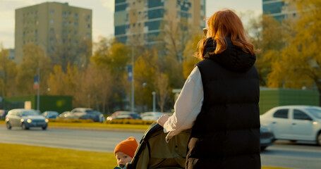 Young redheaded mother walks with baby stroller through city streets in autumn