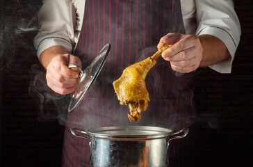 Cook lifts a chicken leg from a pot of boiling water in a busy kitchen. Steam rises as the cook prepares the dish with a focus on the cooking process