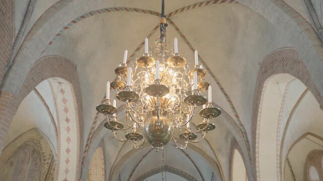 A stunning chandelier hangs from a beautifully designed ceiling, showcasing intricate architectural details. The interplay of light and shadows enhances the ambiance of the space, blending elegance an