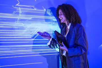 Professional female tech expert interacting with artificial intelligence interface. Woman developer using tablet to analyze digital circuit board data on blue screen.