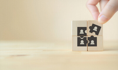 Hand placing puzzle piece with human icon into wooden block with people icons  teamwork concept