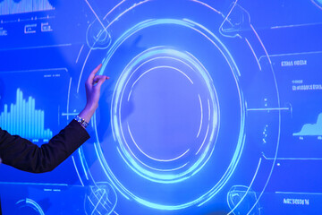 Business executive presenting digital strategy on large blue screen. Female leader pointing at circular data chart during corporate meeting presentation at night.