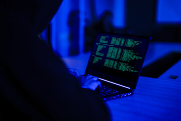 Professional cyber security specialist monitoring network safety. Tech expert in hoodie analyzing code to protect digital system from hacker threats in dark office.