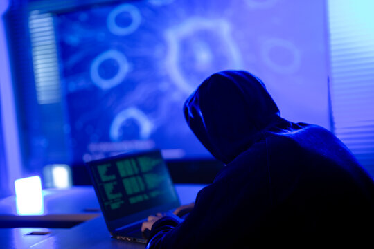 Hardworking software developer writing complex code on laptop at night. Freelance programmer working late on new digital project in modern dark blue workspace.