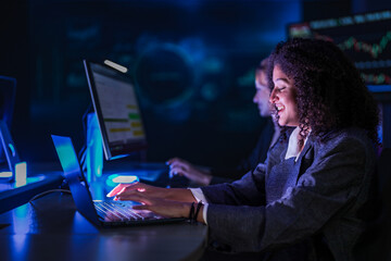 Cyber security analysts monitoring network data on digital display. Female tech experts discussing system defense strategy in dark control room center at night.