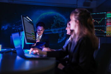 Professional female traders analyzing stock market trends. Business team monitoring financial investment growth graphs on computer screens in modern night office.