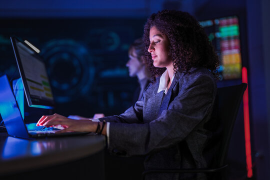 Cyber security analysts monitoring network data on digital display. Female tech experts discussing system defense strategy in dark control room center at night. - Powered by Adobe