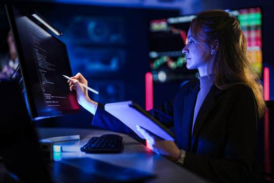 Cyber security specialist monitoring global network safety. Female tech expert typing code to protect digital system from threats in dark blue control room at night. - Powered by Adobe