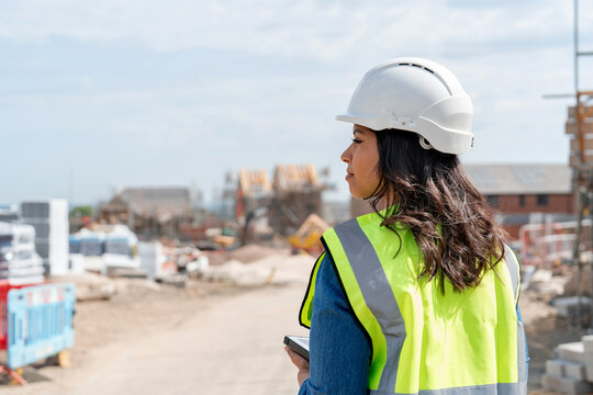 Young woman builder construction manager uses rugged tablet to record data on construction site