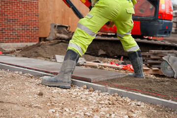 Skilled builder laying concrete paving slabs on sand and cement mix for new pathway