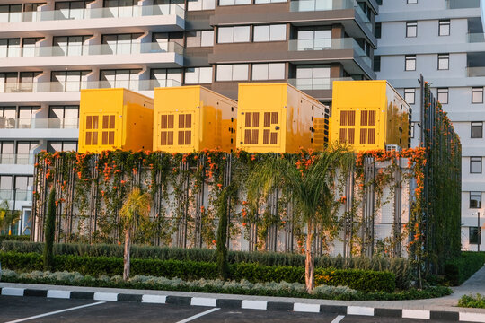 Yellow industrial generators installed on a landscaped platform in a modern residential complex in Cyprus, showing urban infrastructure, backup power systems and contemporary city development.
