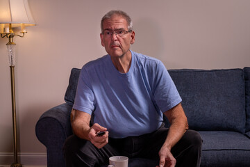 Fototapeta premium Older man watching TV with intent in a dimly lit room