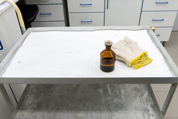 Laboratory transport trolley made of metal, with two shelves. White protective paper on the top shelf, various laboratory items on it.